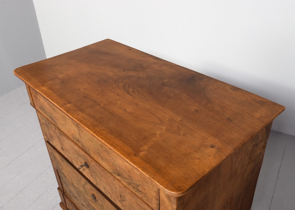 A Biedermeier chest of drawers constructed from figured blonde walnut veneer with four drawers and block feet. View II