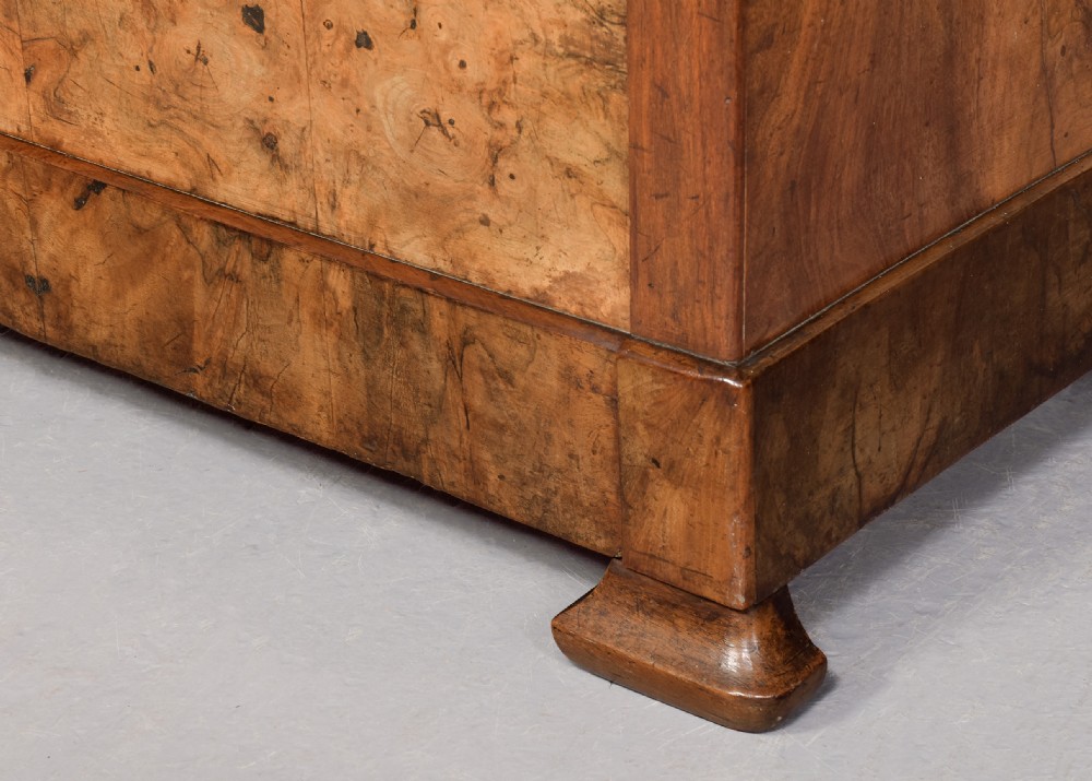 A Biedermeier chest of drawers constructed from figured blonde walnut veneer with four drawers and block feet. View IV