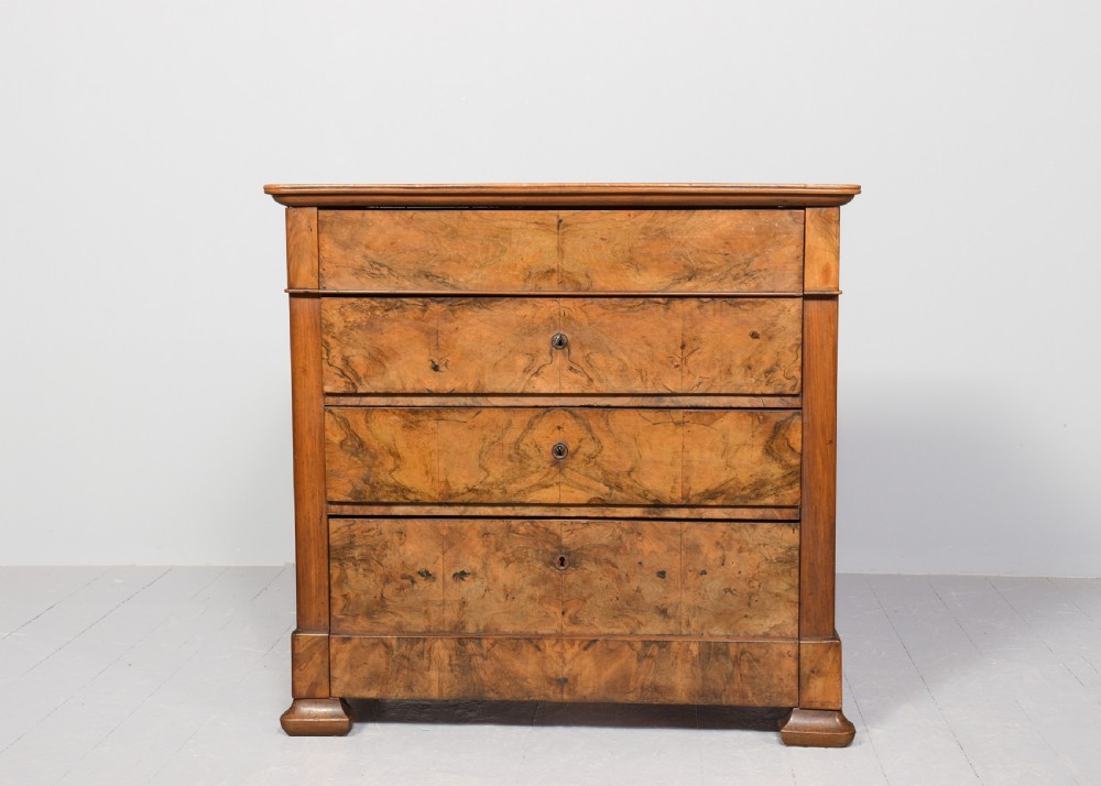 A Biedermeier chest of drawers constructed from figured blonde walnut veneer with four drawers and block feet. View VI