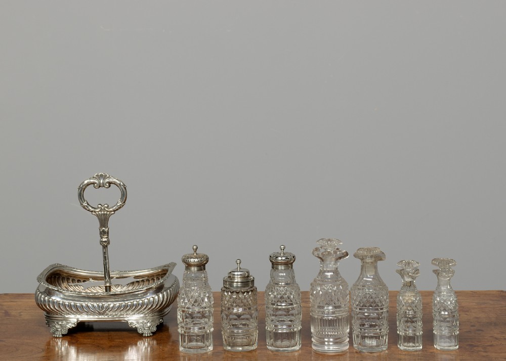 A Regency solid silver cruet stand featuring six cut-glass bottles with silver tops, supported by a gadrooned frame with a central loop handle and paw feet. View IV