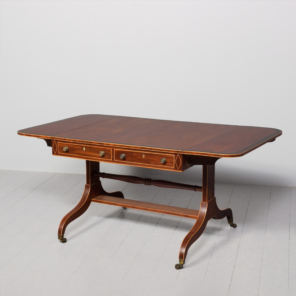 A Regency mahogany sofa table featuring drop flaps, geometric string inlay, twin frieze drawers, and splayed legs with brass castors. View II