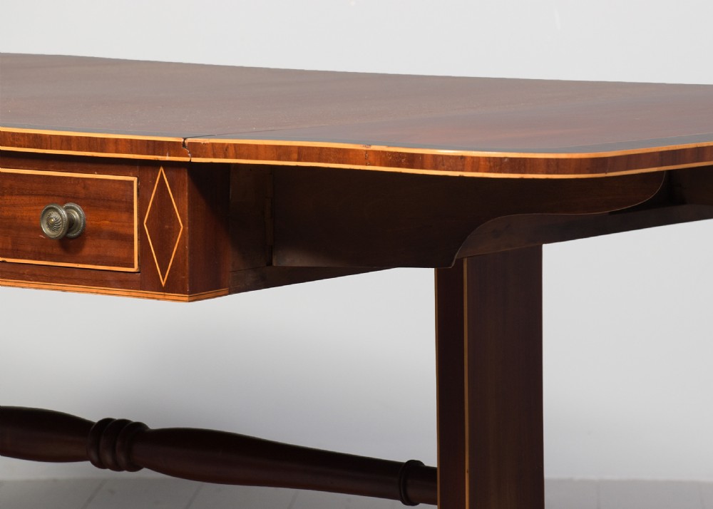 A Regency mahogany sofa table featuring drop flaps, geometric string inlay, twin frieze drawers, and splayed legs with brass castors. View VII