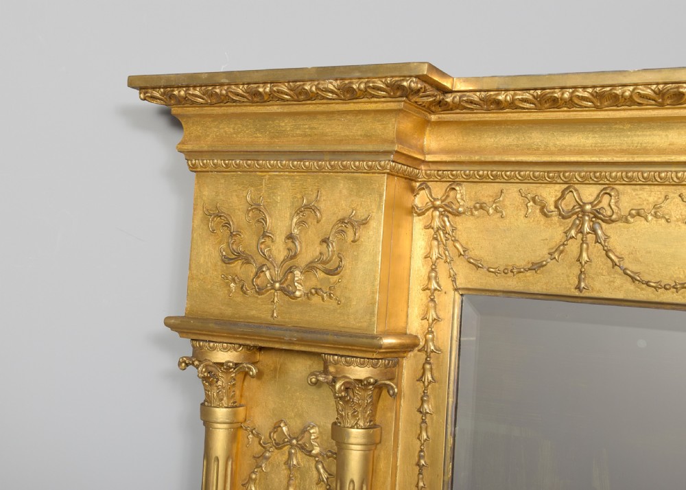 A large 19th-century Neoclassical giltwood overmantel mirror featuring classical column pilasters, ribbon festoon mouldings, and a heavy breakfront cornice. View II
