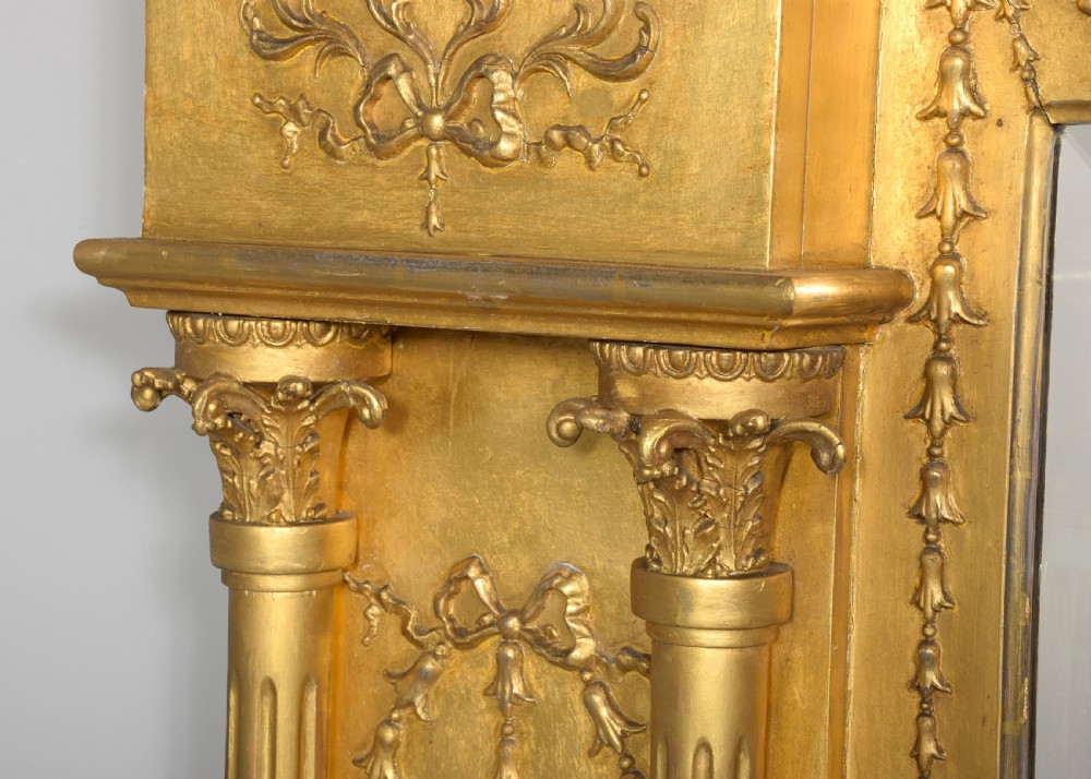A large 19th-century Neoclassical giltwood overmantel mirror featuring classical column pilasters, ribbon festoon mouldings, and a heavy breakfront cornice. View III