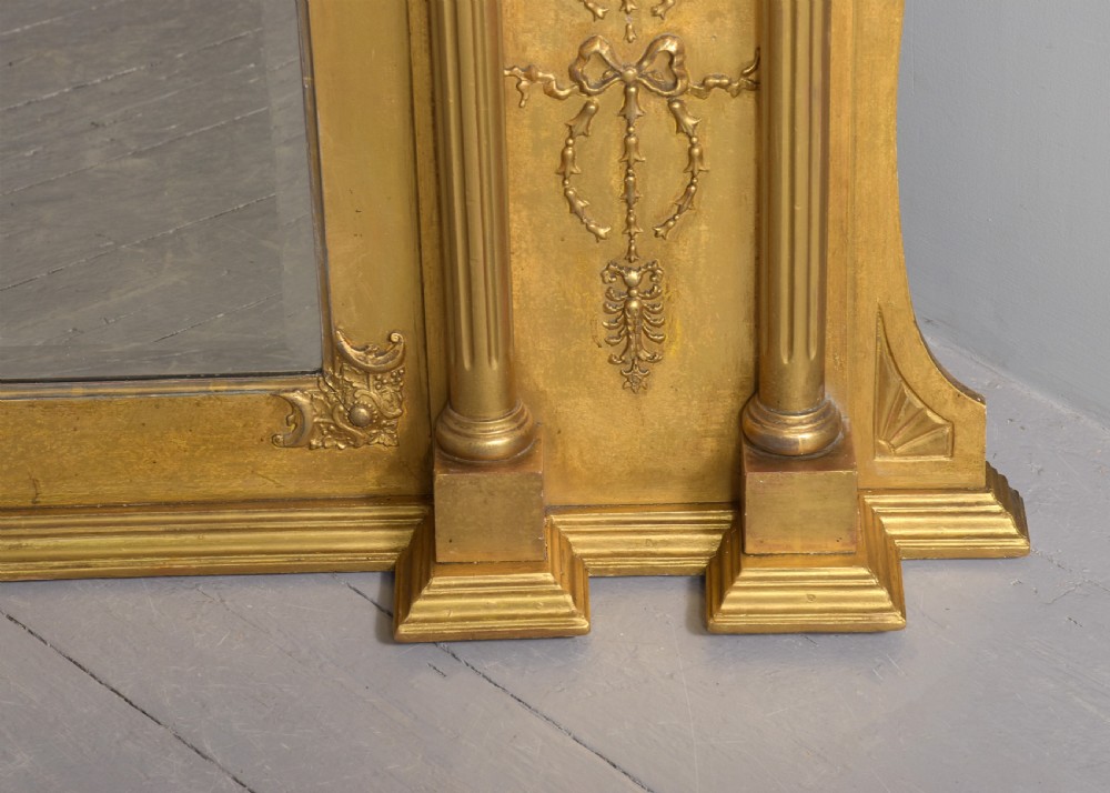 A large 19th-century Neoclassical giltwood overmantel mirror featuring classical column pilasters, ribbon festoon mouldings, and a heavy breakfront cornice. View IV