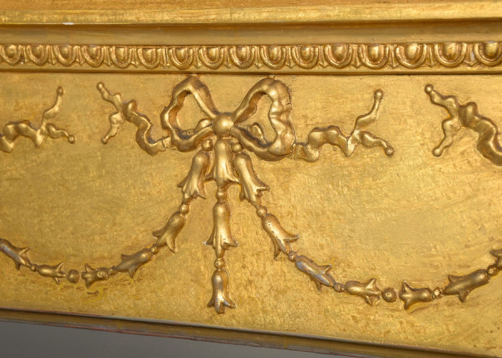 A large 19th-century Neoclassical giltwood overmantel mirror featuring classical column pilasters, ribbon festoon mouldings, and a heavy breakfront cornice. View VII