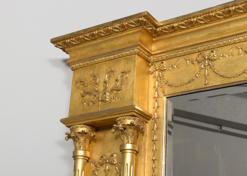 A large 19th-century Neoclassical giltwood overmantel mirror featuring classical column pilasters, ribbon festoon mouldings, and a heavy breakfront cornice. View VIII