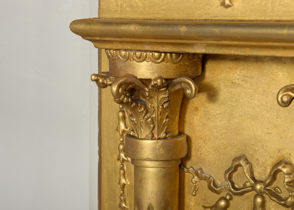 A large 19th-century Neoclassical giltwood overmantel mirror featuring classical column pilasters, ribbon festoon mouldings, and a heavy breakfront cornice. View IX