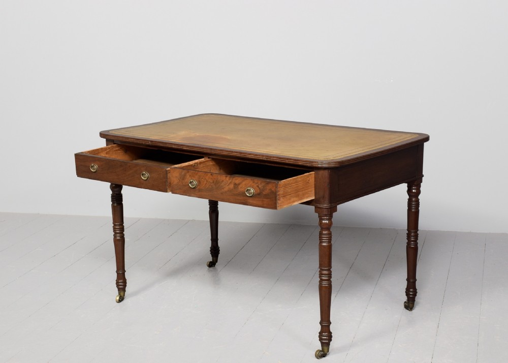 A George III mahogany library table featuring a tan leather writing surface, two frieze drawers with brass ring pulls, turned legs, and brass castors. View IV