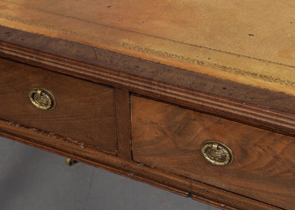 A George III mahogany library table featuring a tan leather writing surface, two frieze drawers with brass ring pulls, turned legs, and brass castors. View VIII