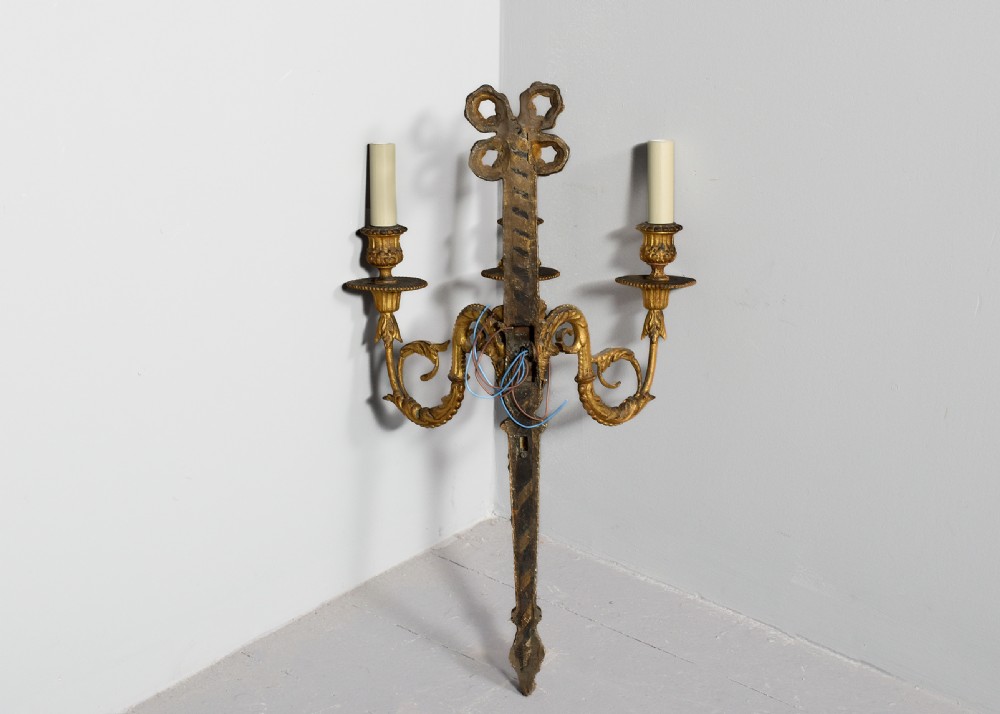 A set of four gilded three-arm wall sconces featuring neoclassical ribbon bow tops and scrolling leaf motifs. View XIII