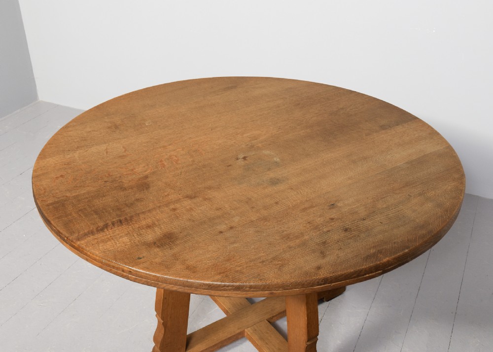 A circular solid oak dining table with a cross-shaped cruciform base and natural wood grain finish. View II