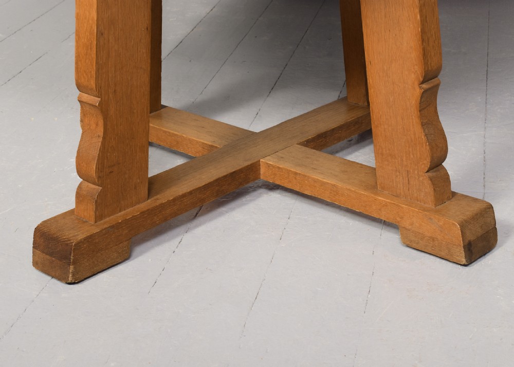 A circular solid oak dining table with a cross-shaped cruciform base and natural wood grain finish. View IV
