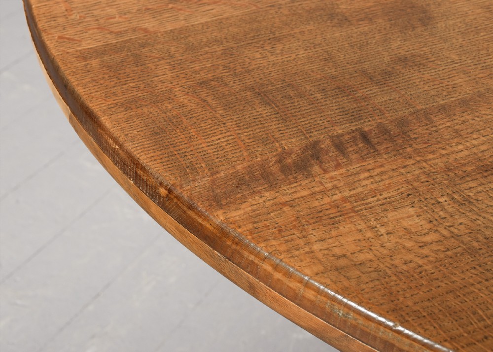 A circular solid oak dining table with a cross-shaped cruciform base and natural wood grain finish. View V