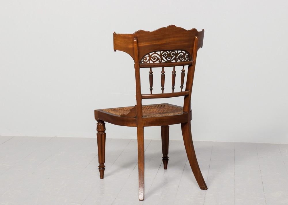 A carved mahogany side chair featuring a wide curved crest rail, pierced fretwork back, cushioned cane seat, and reeded front legs. View V
