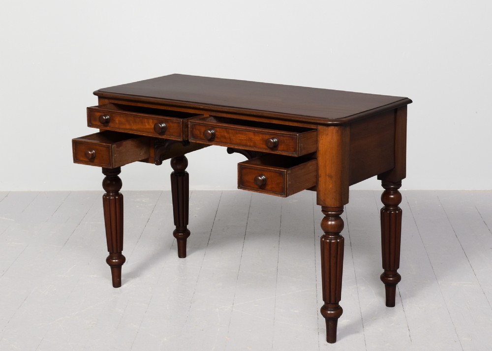 A George IV mahogany writing table featuring four drawers with wooden turned handles, carved corner spandrels, and reeded turned legs. View III
