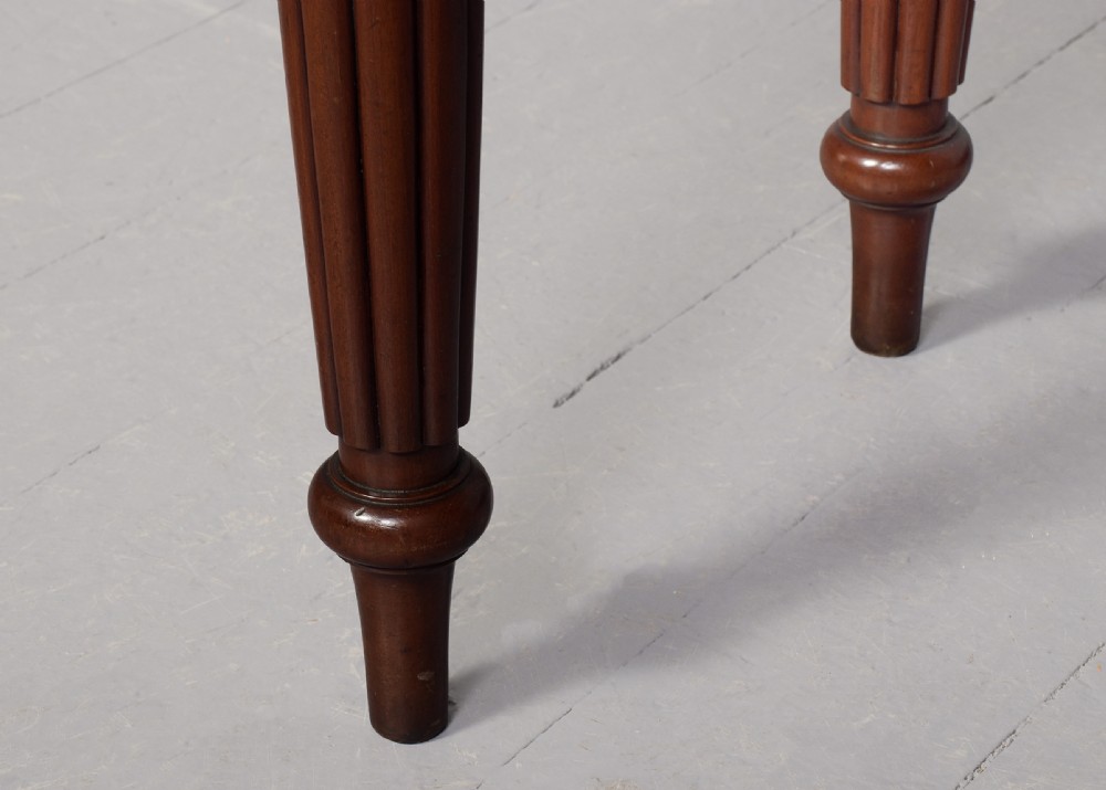 A George IV mahogany writing table featuring four drawers with wooden turned handles, carved corner spandrels, and reeded turned legs. View VII