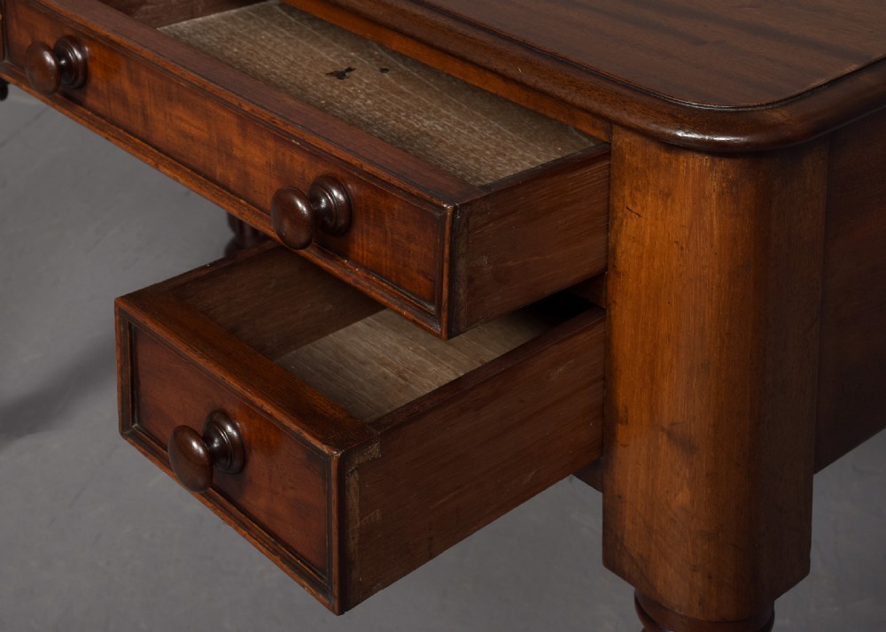 A George IV mahogany writing table featuring four drawers with wooden turned handles, carved corner spandrels, and reeded turned legs. View IX