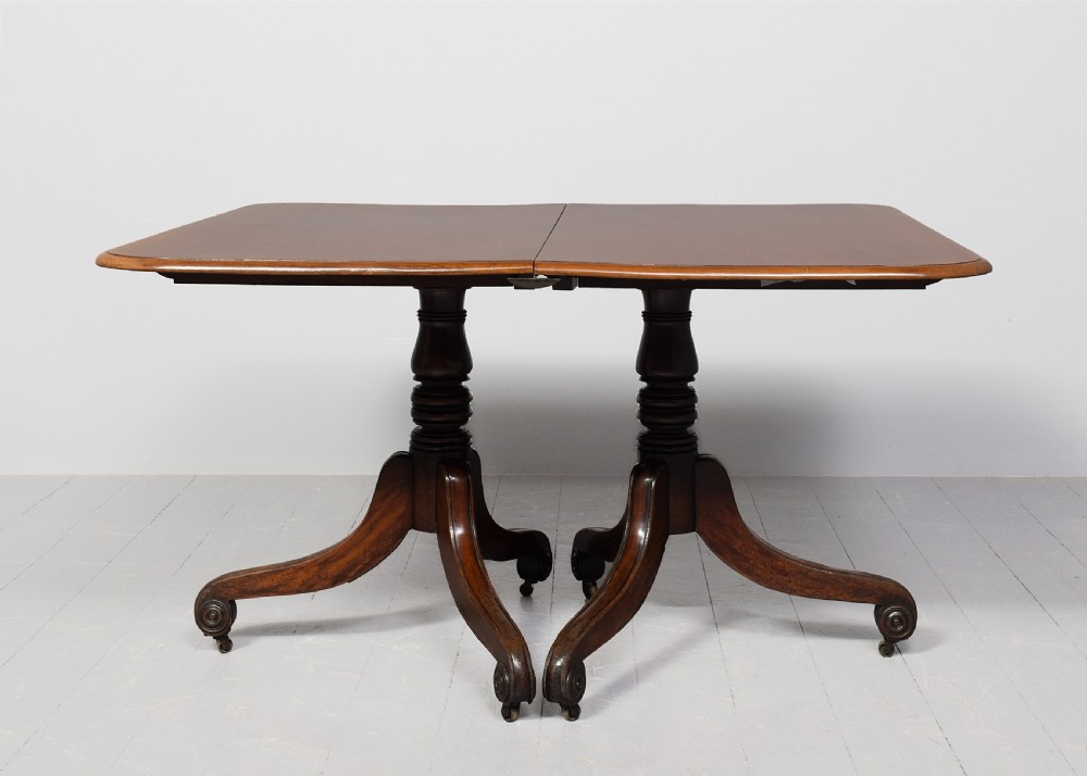 A George IV mahogany twin pillar extendable dining table with a central leaf, supported on turned columns and splayed legs with brass castors. View II