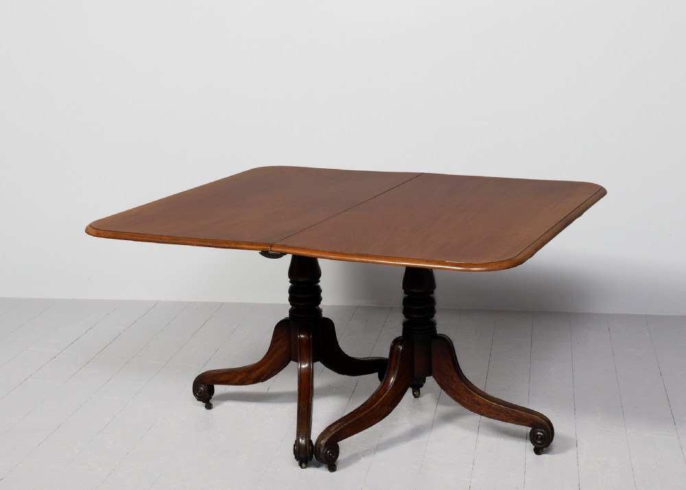 A George IV mahogany twin pillar extendable dining table with a central leaf, supported on turned columns and splayed legs with brass castors. View VI