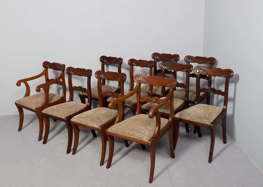A set of ten Scottish carved mahogany dining chairs featuring cresting bar backs, carved splats, neutral fabric seats, and curved sabre front legs. View II