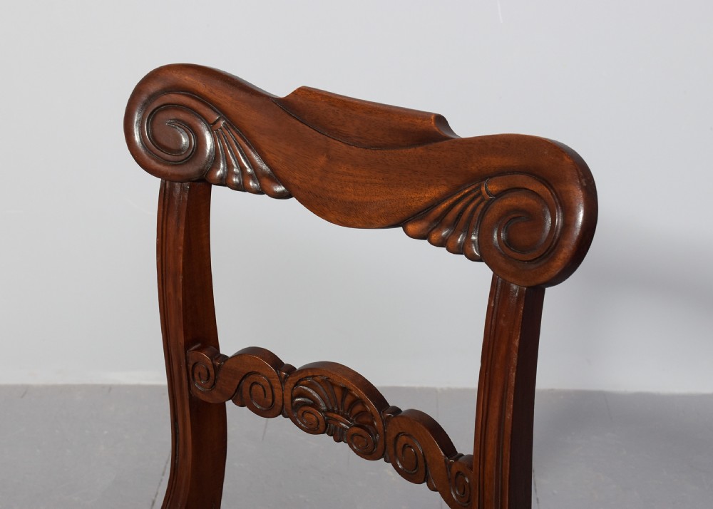 A set of ten Scottish carved mahogany dining chairs featuring cresting bar backs, carved splats, neutral fabric seats, and curved sabre front legs. View IV
