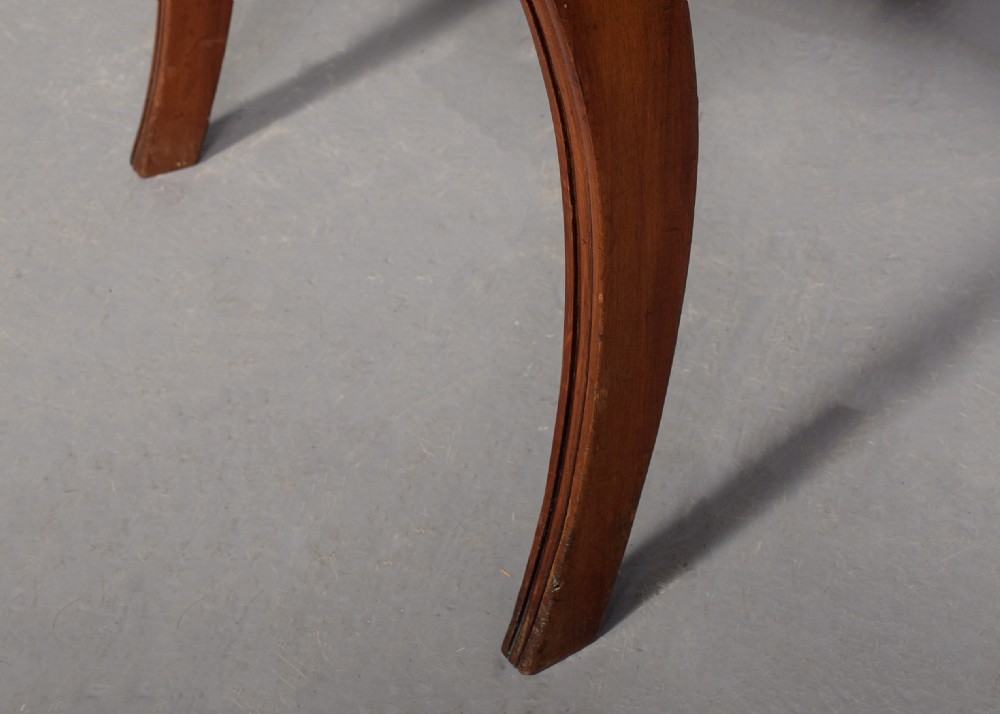 A set of ten Scottish carved mahogany dining chairs featuring cresting bar backs, carved splats, neutral fabric seats, and curved sabre front legs. View V