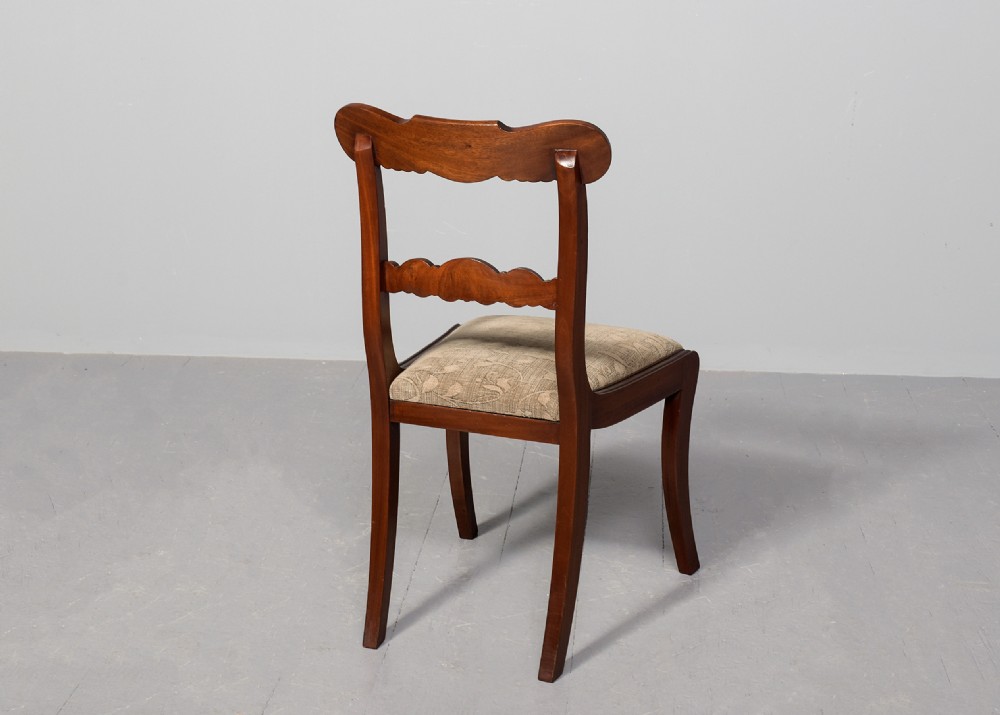 A set of ten Scottish carved mahogany dining chairs featuring cresting bar backs, carved splats, neutral fabric seats, and curved sabre front legs. View VI