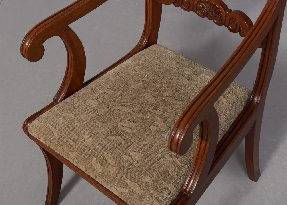 A set of ten Scottish carved mahogany dining chairs featuring cresting bar backs, carved splats, neutral fabric seats, and curved sabre front legs. View IX