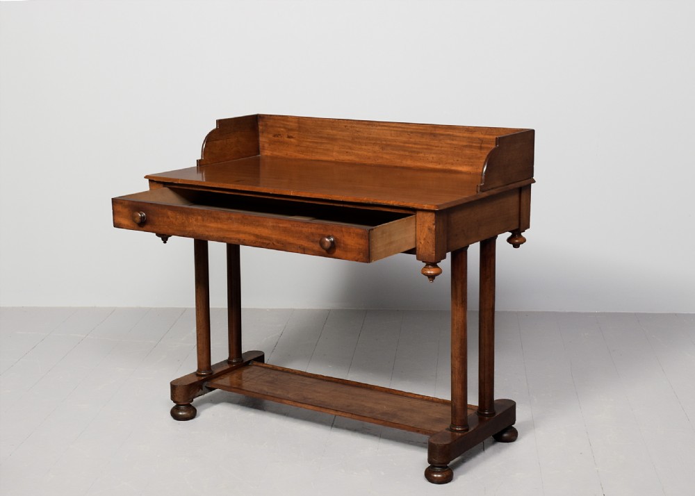 A William IV mahogany side table featuring a low gallery upstand, a long frieze drawer with round wooden knobs, twin turned end supports, a low stretcher, and bun feet. View III
