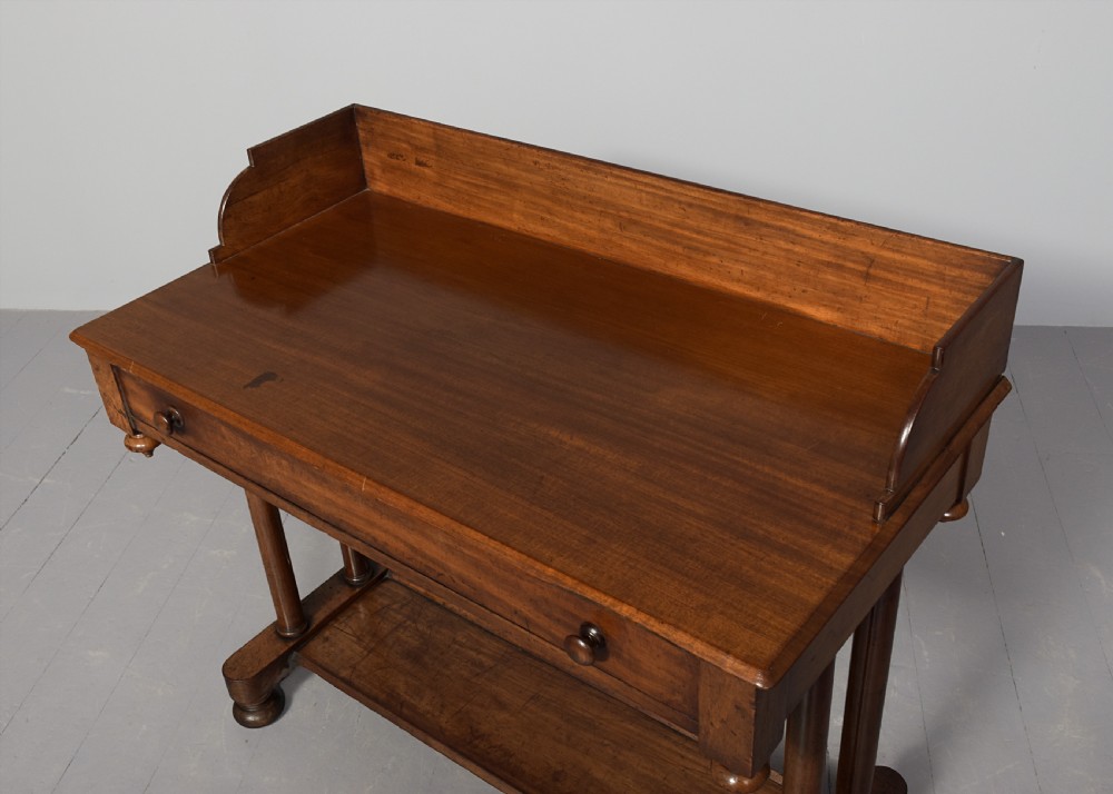 A William IV mahogany side table featuring a low gallery upstand, a long frieze drawer with round wooden knobs, twin turned end supports, a low stretcher, and bun feet. View IV