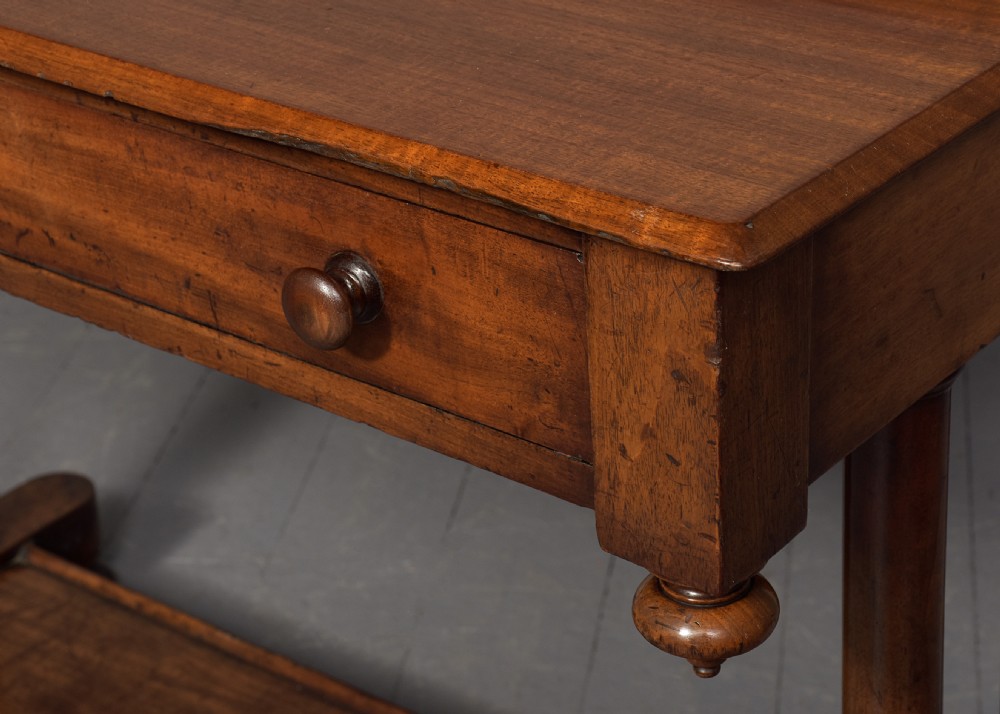A William IV mahogany side table featuring a low gallery upstand, a long frieze drawer with round wooden knobs, twin turned end supports, a low stretcher, and bun feet. View V