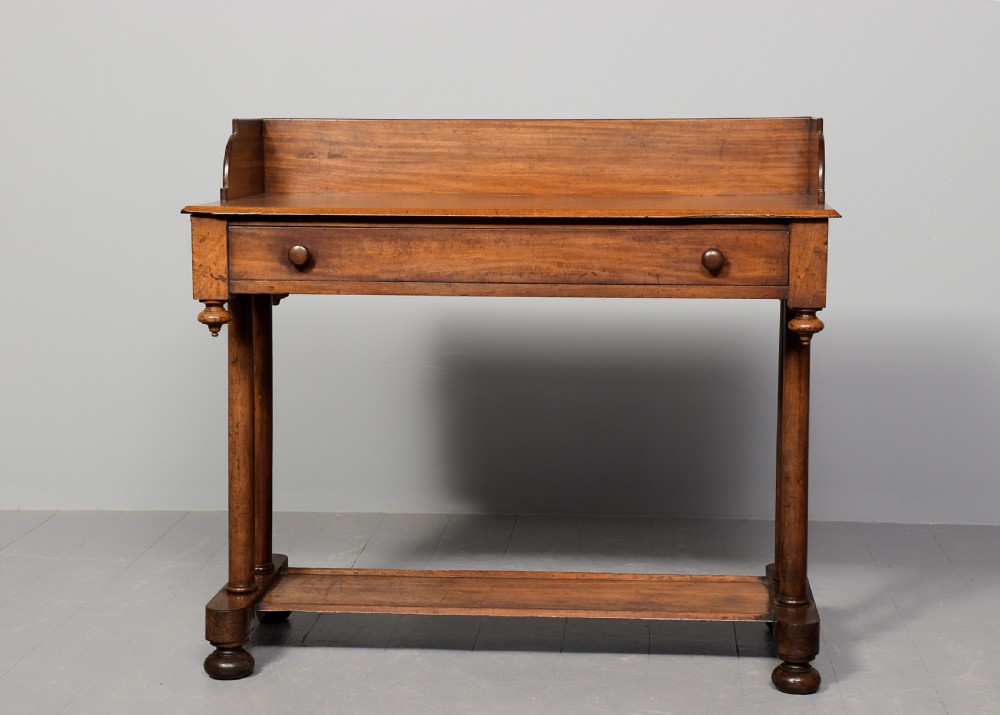 A William IV mahogany side table featuring a low gallery upstand, a long frieze drawer with round wooden knobs, twin turned end supports, a low stretcher, and bun feet. View VII