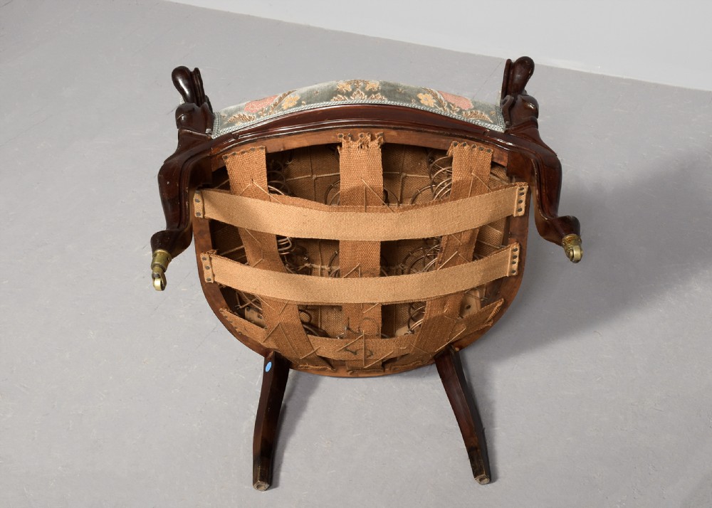 A pair of Victorian rosewood armchairs featuring carved cresting rails, padded armrests, floral patterned textile upholstery, and cabriole legs on brass castors. View X