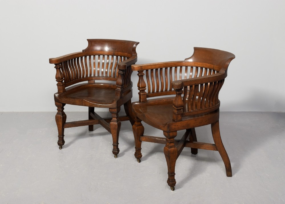 A set of four Victorian dark oak captains chairs featuring curved spindle backs, contoured seats, turned legs, and brass castors. View III