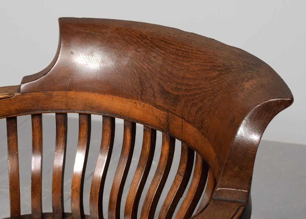A set of four Victorian dark oak captains chairs featuring curved spindle backs, contoured seats, turned legs, and brass castors. View V