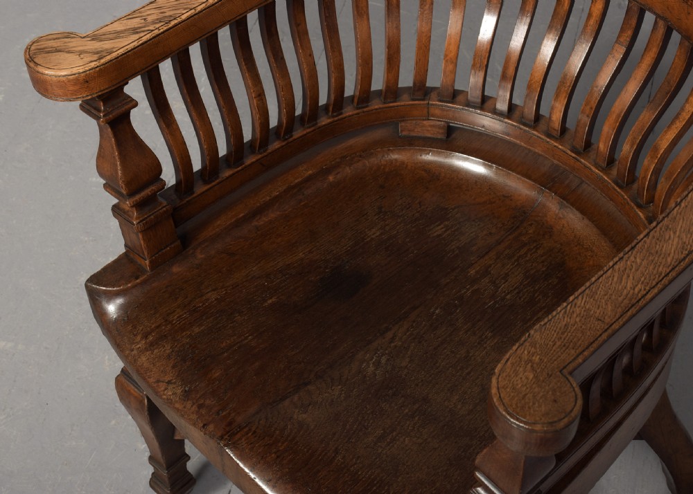 A set of four Victorian dark oak captains chairs featuring curved spindle backs, contoured seats, turned legs, and brass castors. View VI