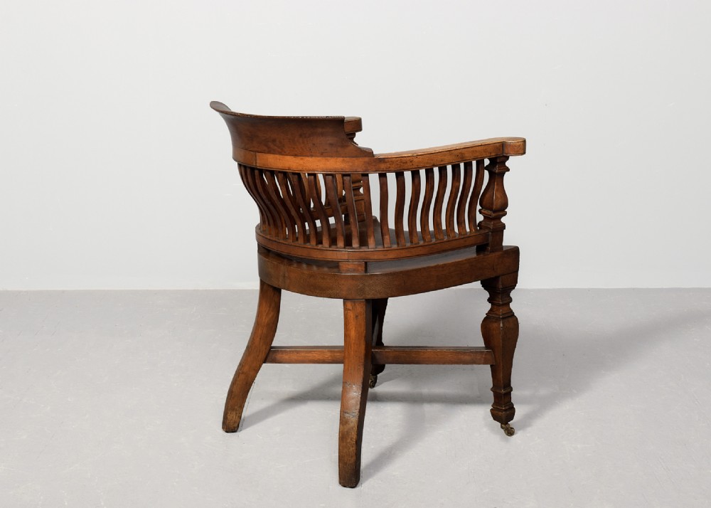 A set of four Victorian dark oak captains chairs featuring curved spindle backs, contoured seats, turned legs, and brass castors. View VIII