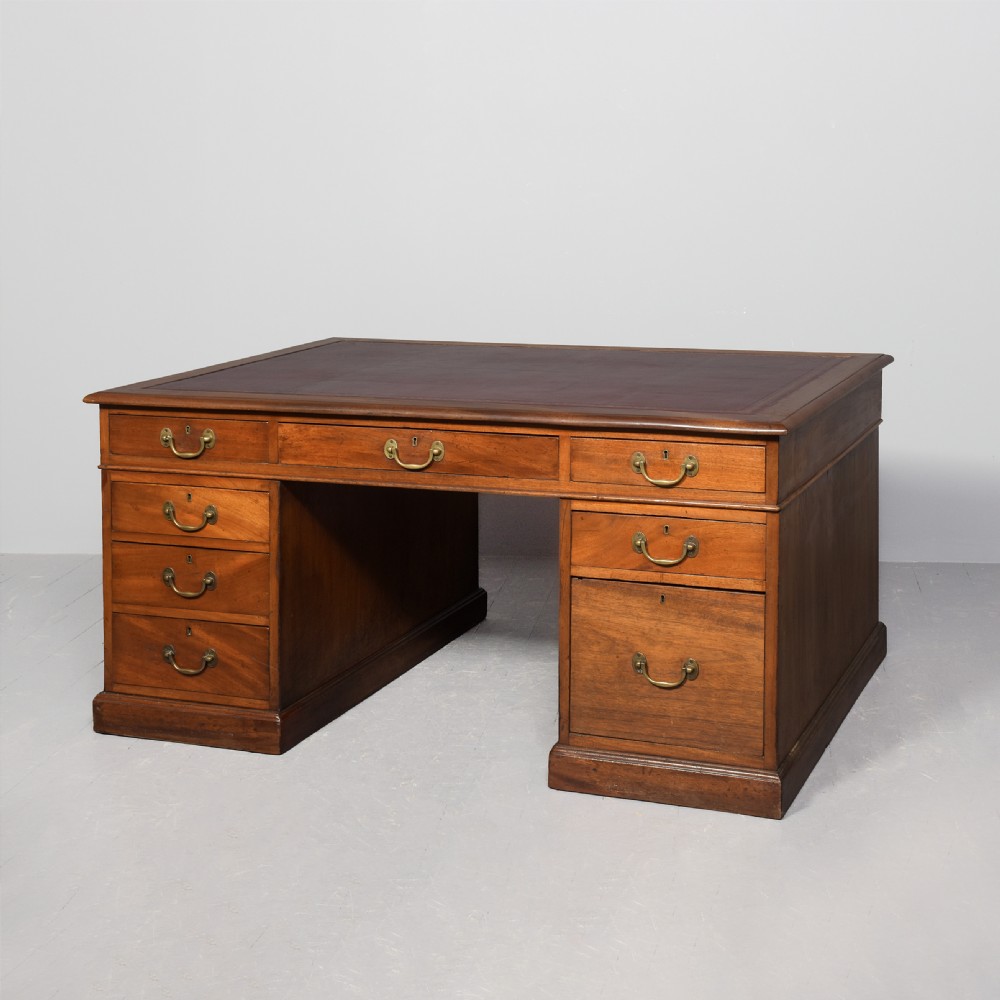 A large Victorian mahogany partners desk with a brown leather inset writing surface, twin pedestals with drawers, and brass swan-neck drop handles.