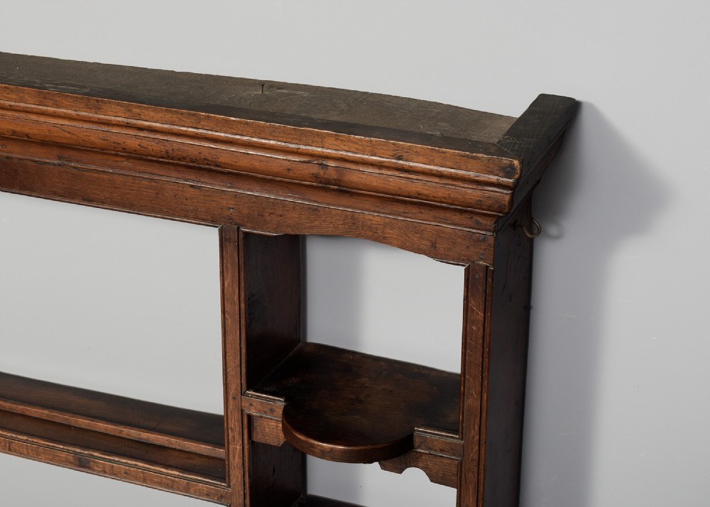 An 18th-century George III dark oak wall rack featuring a moulded cornice, three open central shelves, and vertical side compartments. View II