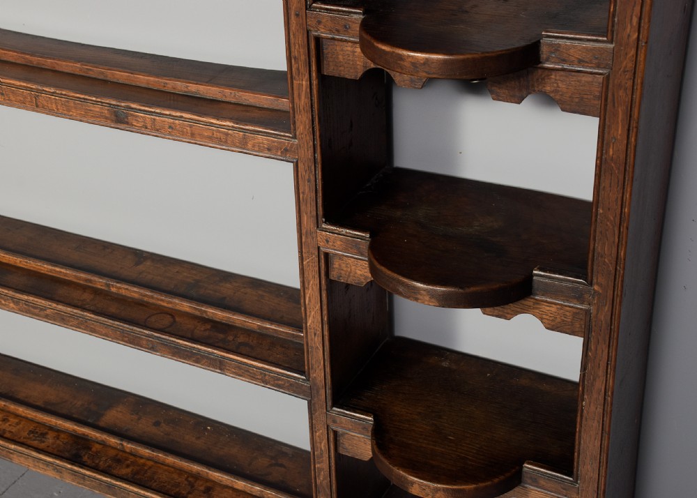 An 18th-century George III dark oak wall rack featuring a moulded cornice, three open central shelves, and vertical side compartments. View III
