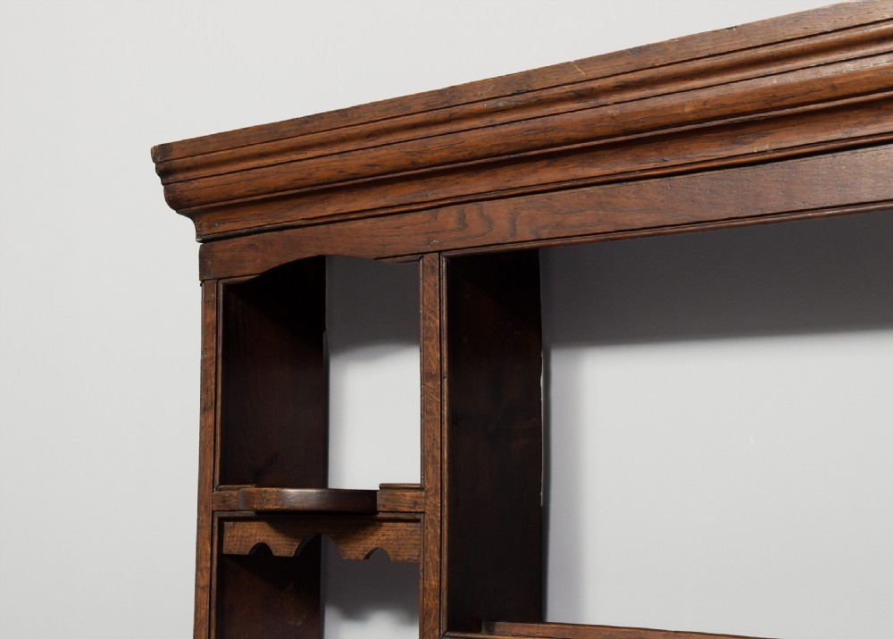 An 18th-century George III dark oak wall rack featuring a moulded cornice, three open central shelves, and vertical side compartments. View V