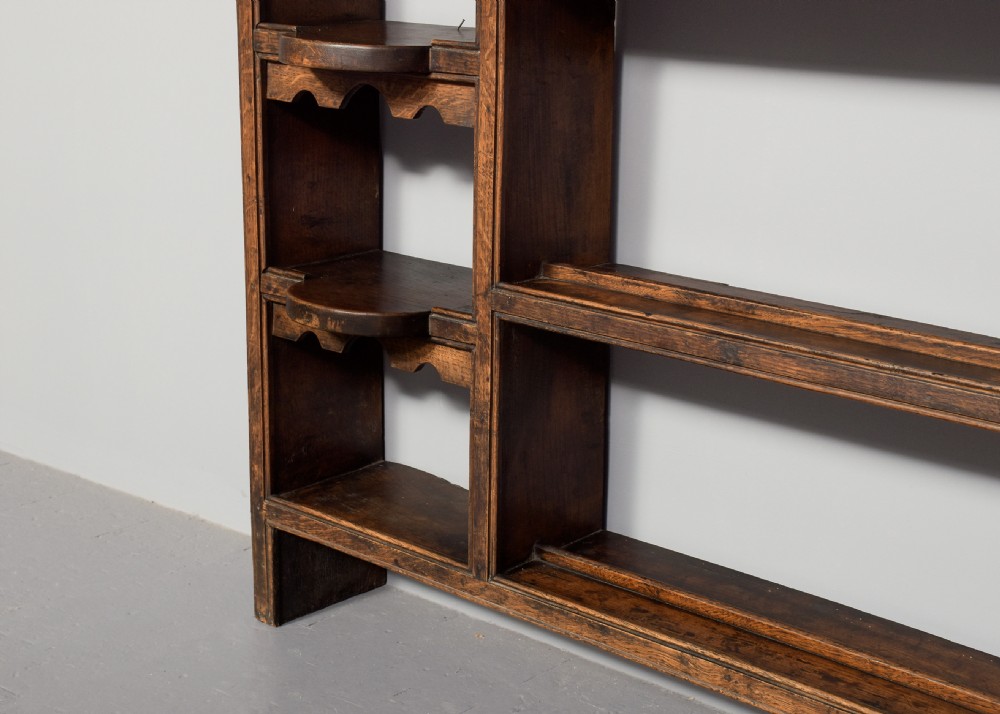 An 18th-century George III dark oak wall rack featuring a moulded cornice, three open central shelves, and vertical side compartments. View VI