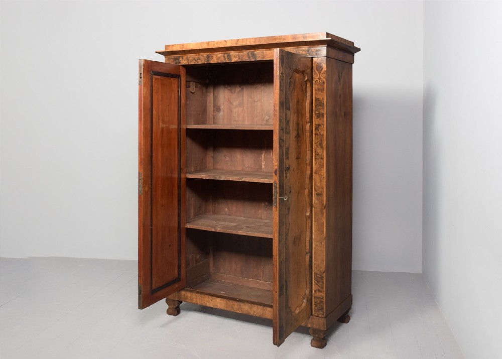 A tall two-door freestanding armoire in figured walnut veneer with shaped door panels, a straight moulded cornice, and plinth base with bracket feet. View VII