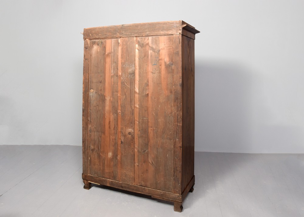 A tall two-door freestanding armoire in figured walnut veneer with shaped door panels, a straight moulded cornice, and plinth base with bracket feet. View X