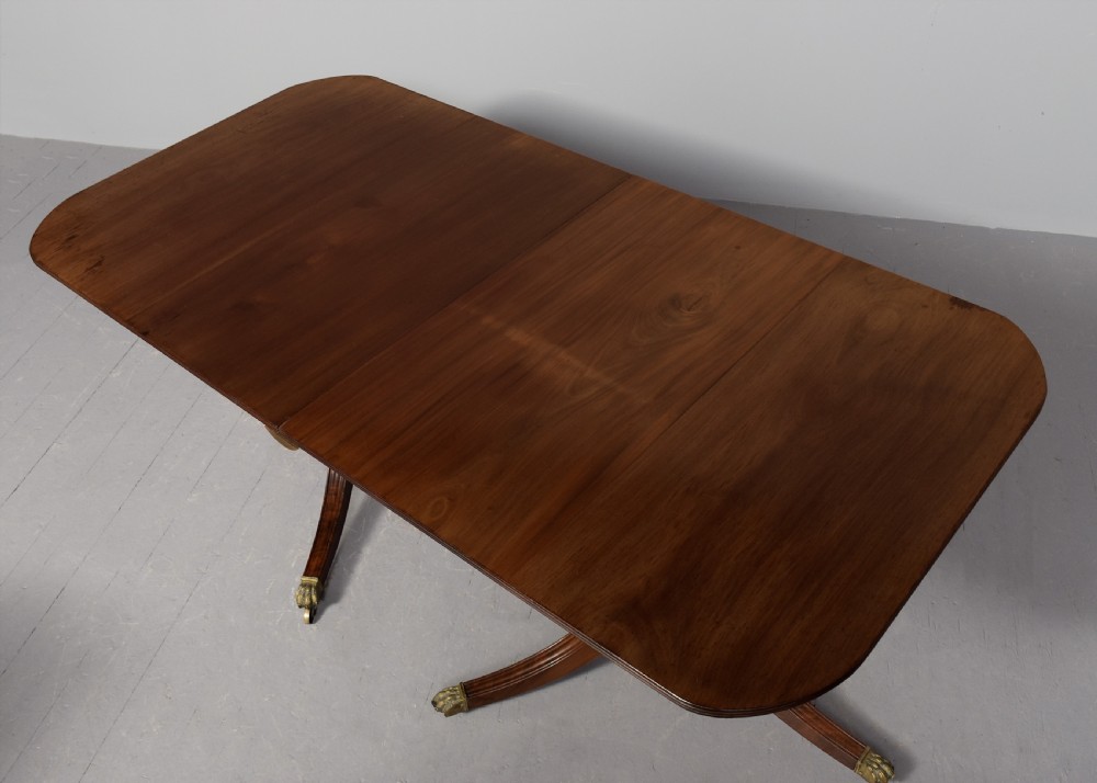 A Georgian style twin pedestal dining table crafted from dark brown Spanish mahogany featuring splayed legs with brass castors and a removable central leaf. View II