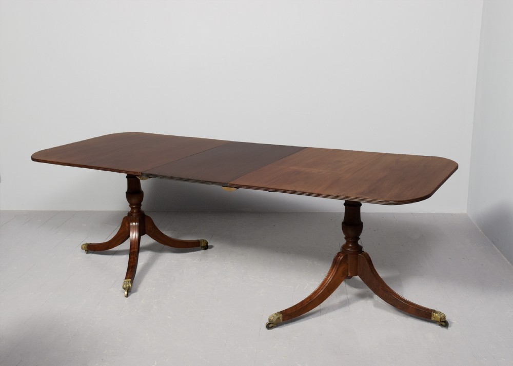 A Georgian style twin pedestal dining table crafted from dark brown Spanish mahogany featuring splayed legs with brass castors and a removable central leaf. View VI