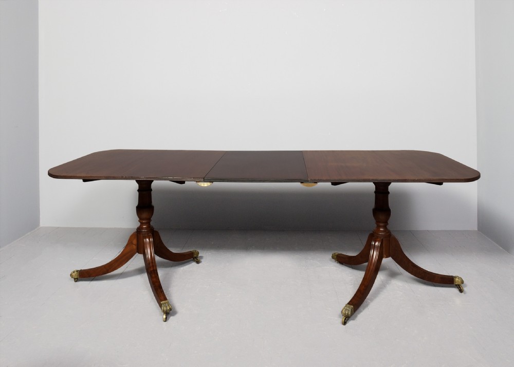 A Georgian style twin pedestal dining table crafted from dark brown Spanish mahogany featuring splayed legs with brass castors and a removable central leaf. View VIII