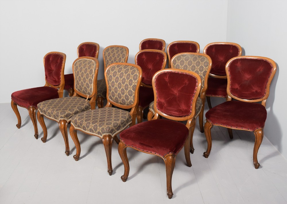 A set of twelve French carved oak dining chairs with balloon backs, cabriole legs, and red velvet or patterned fabric upholstery.