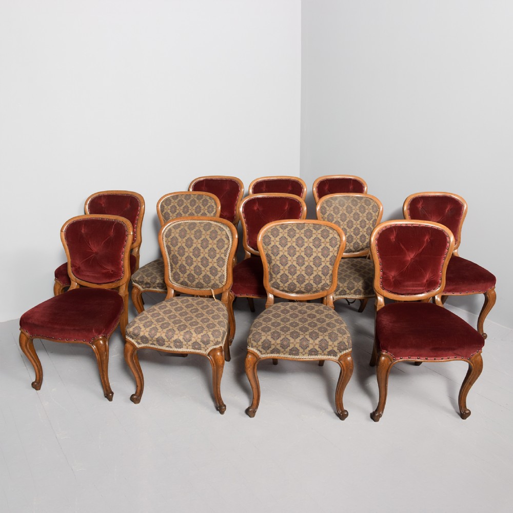 A set of twelve French carved oak dining chairs with balloon backs, cabriole legs, and red velvet or patterned fabric upholstery. View II